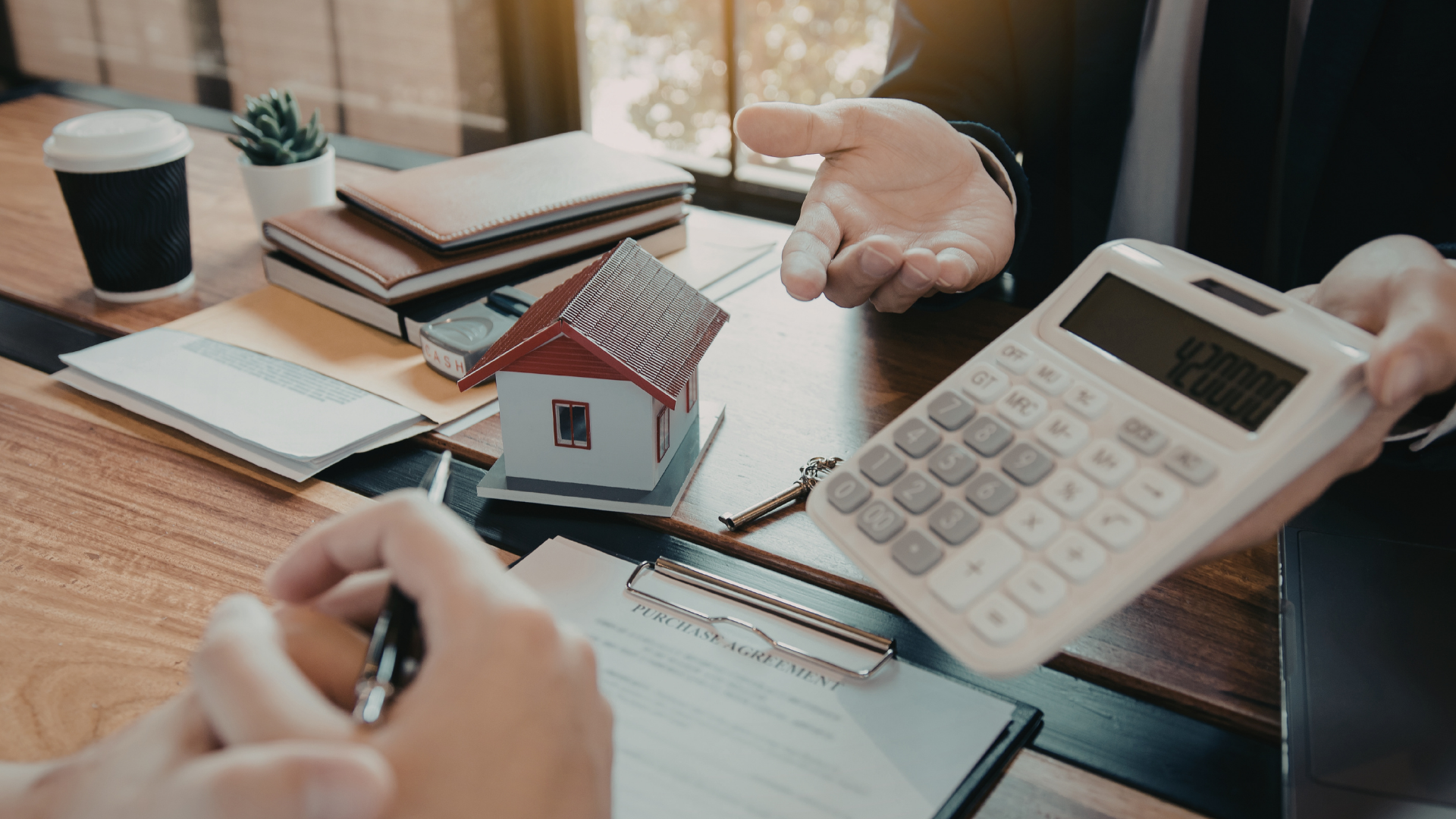 Hands reviewing a house model, calculator, and documents on a desk in a financial planning setting