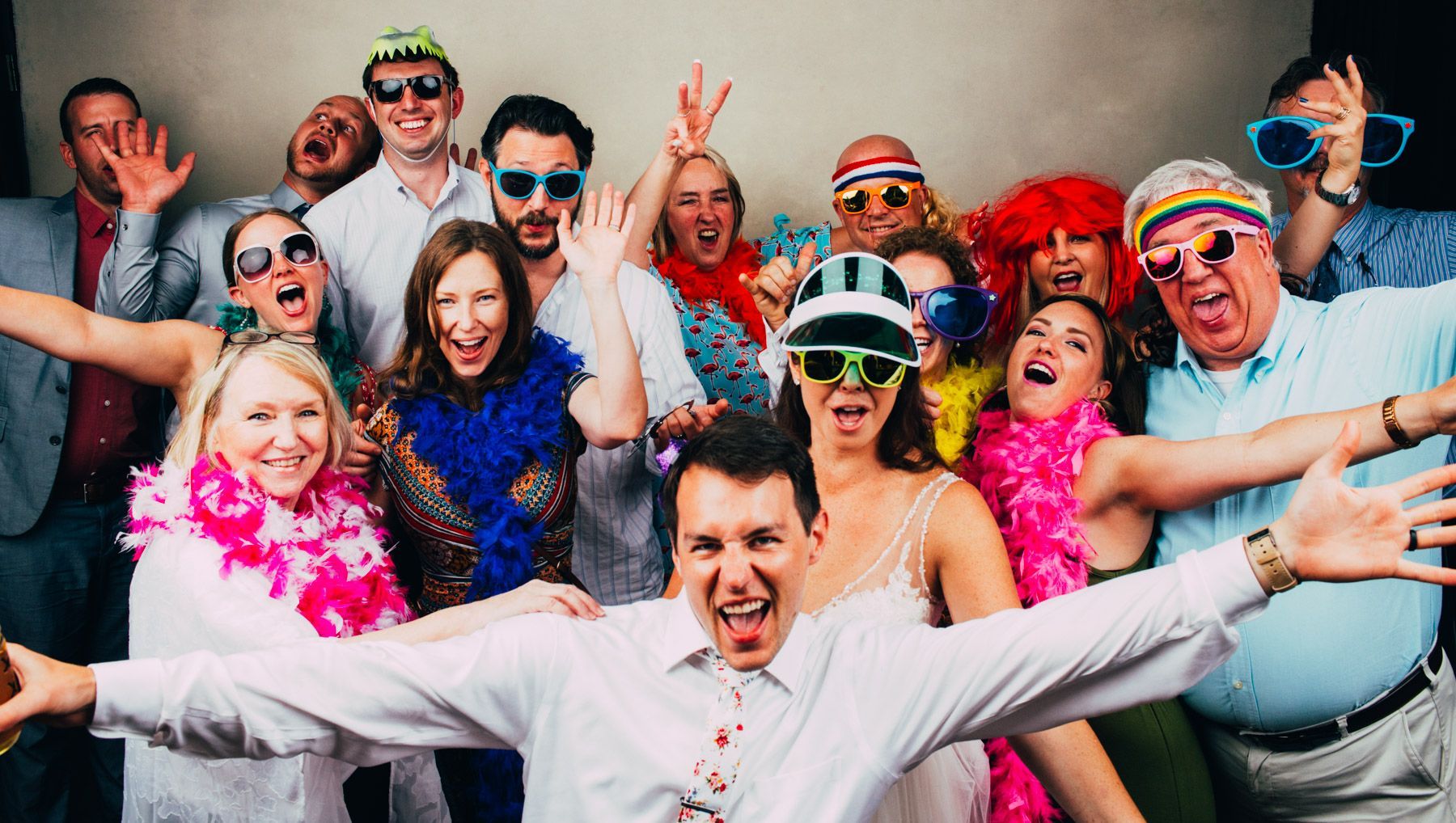 A group of people in colorful sunglasses and leis cheering and posing closely together at a lively party.