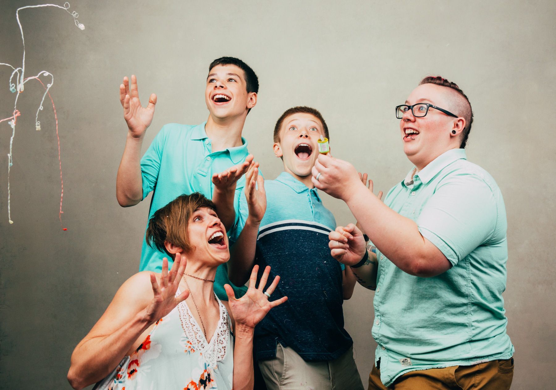 Four people smiling and laughing as colorful powder bursts around them against a chalkboard wall