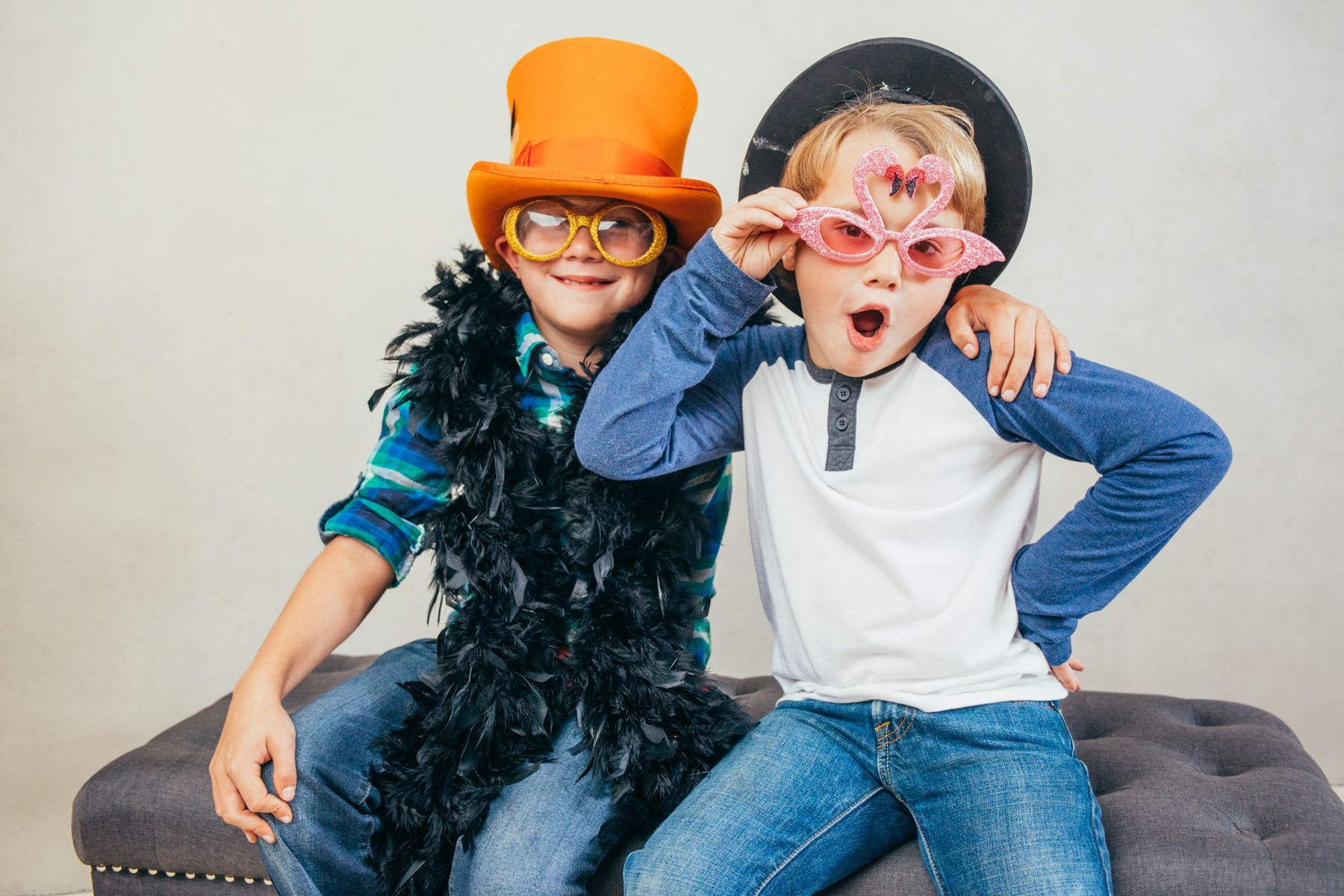 Two children in costumes on a couch, one in an orange hat and glasses, both posing playfully with props