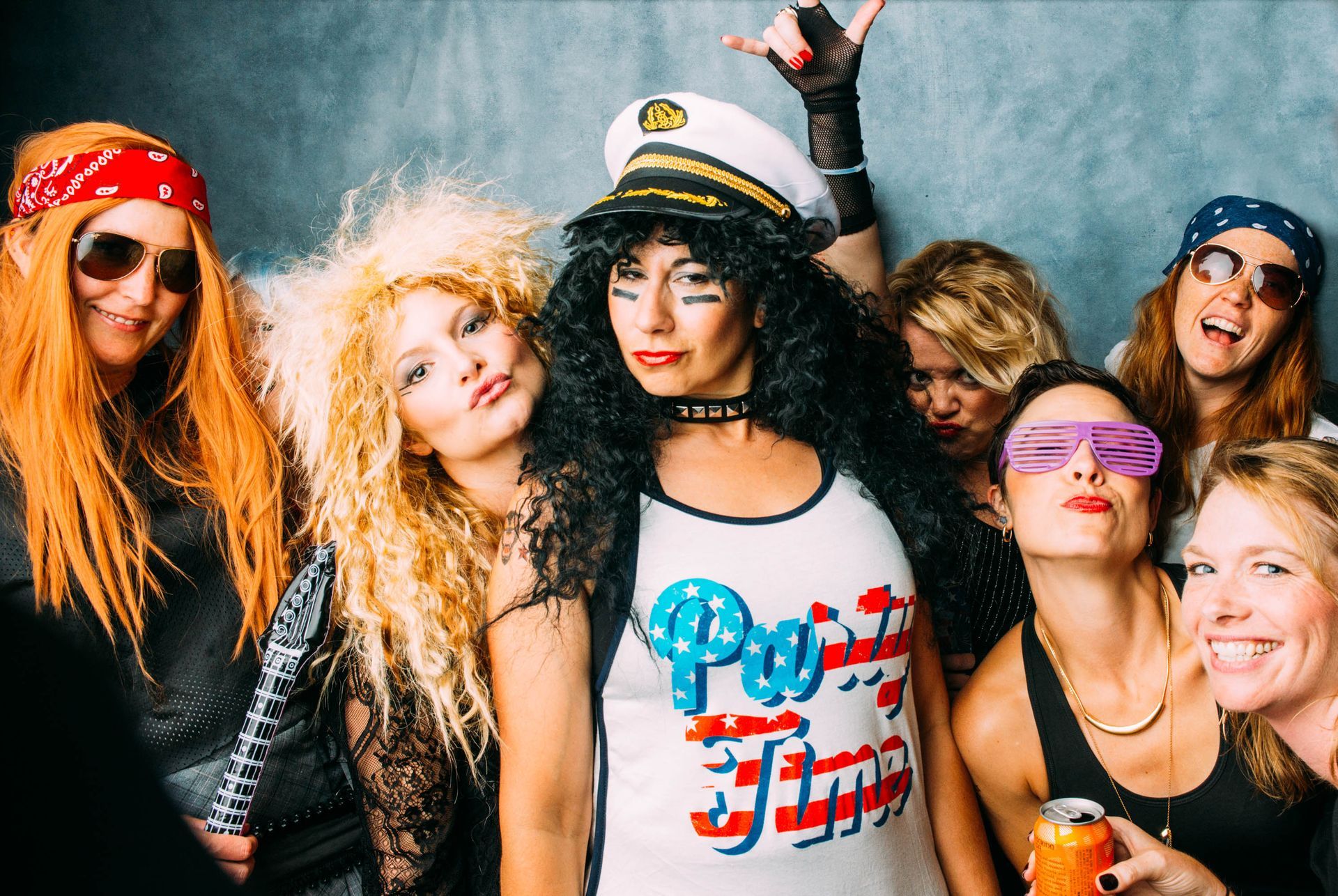 Five friends posing at a lively party, wearing colorful costumes and sunglasses, smiling at the camera.