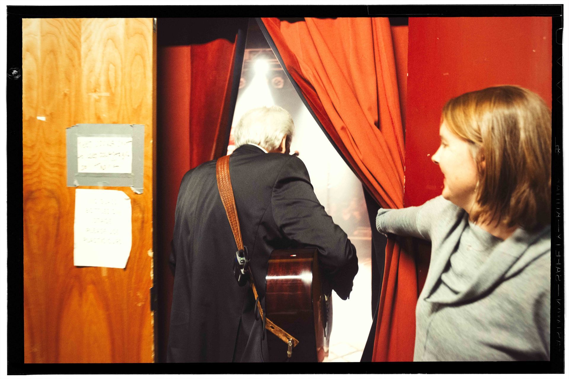 Woman holds open red curtains as an older man enters the stage of the orange peel in Asheville, NC