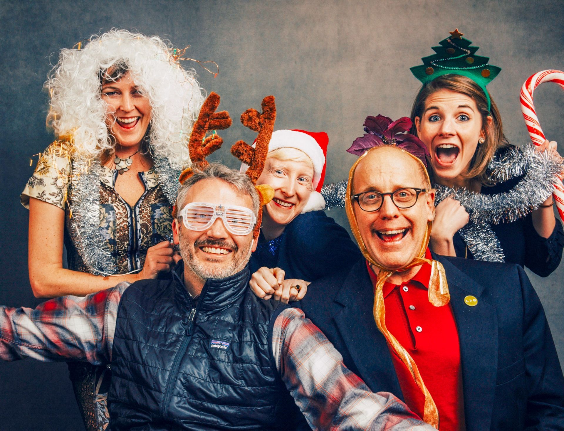 Group of six people in festive costumes smiling and posing with holiday props