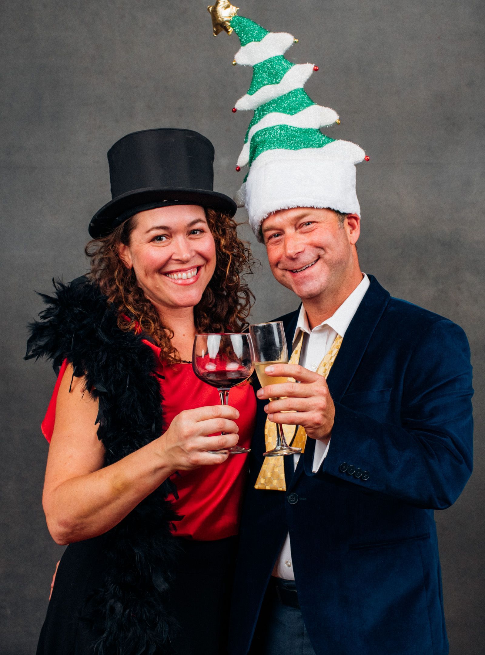 Two people in festive hats toast with wine glasses at a holiday party.