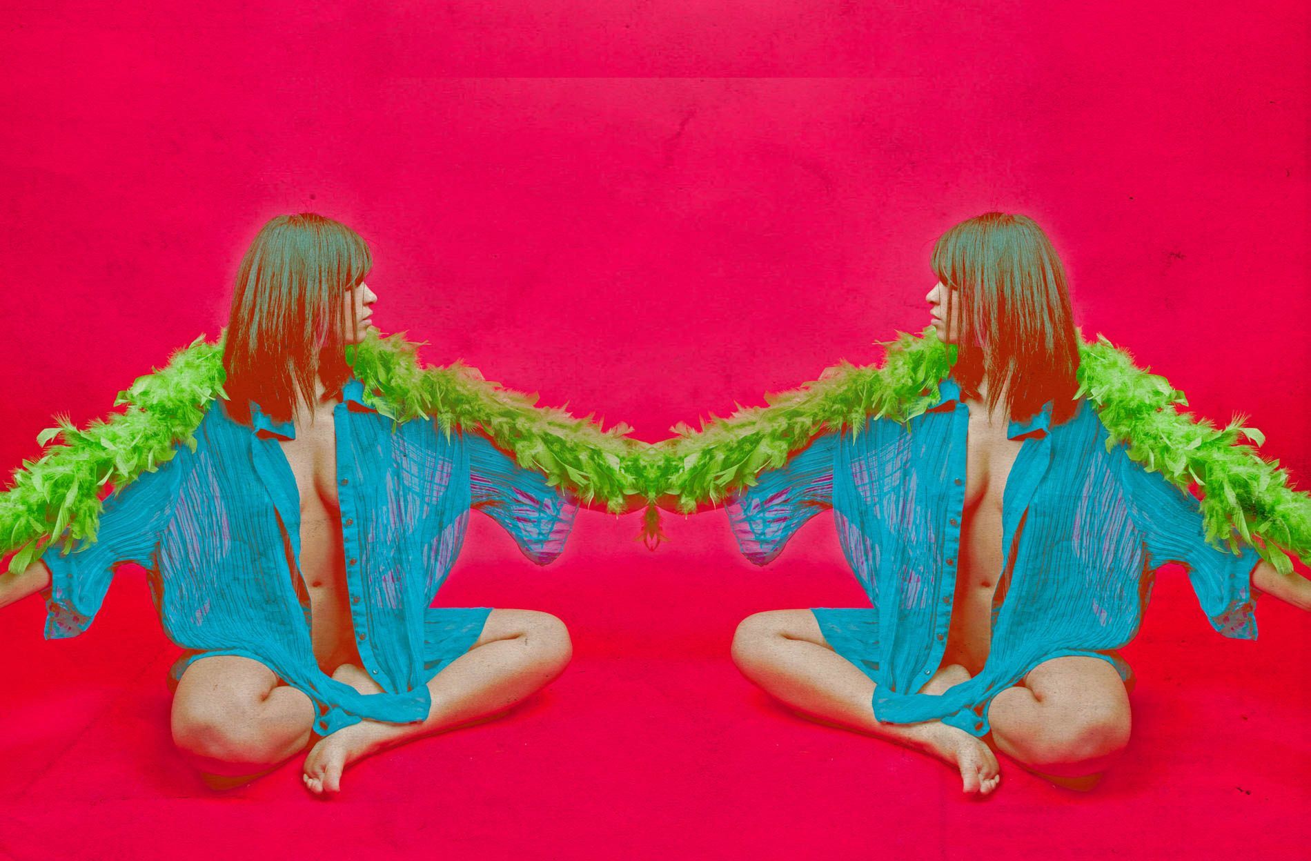 Mirrored person in blue shirt with green feather boa, sitting cross-legged on a bright pink background
