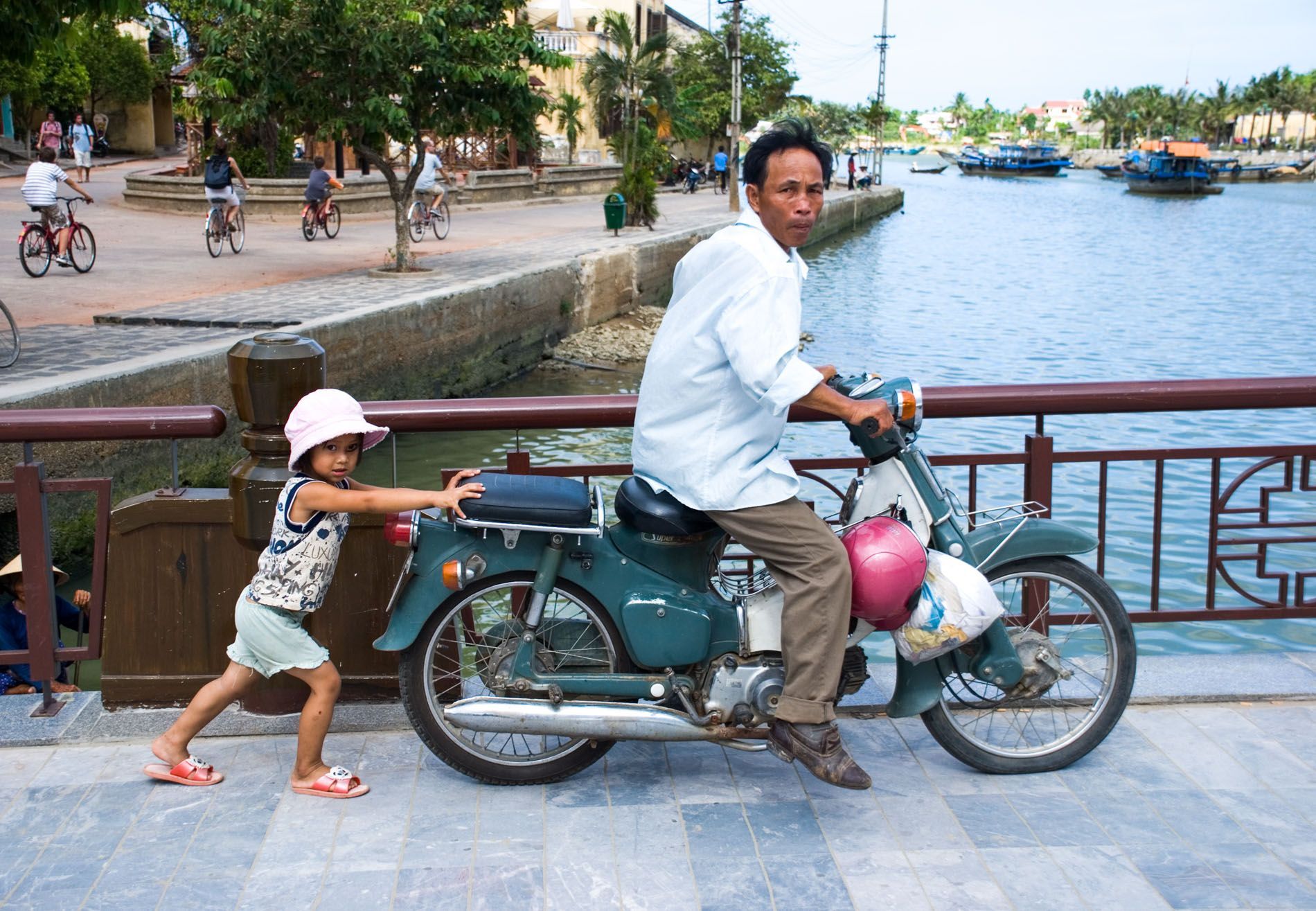 young girl pushes father's motorbike, Hoi An River Central Vietnam, small group travel and food photography tours with Sandlin Gaither Explorer's Club