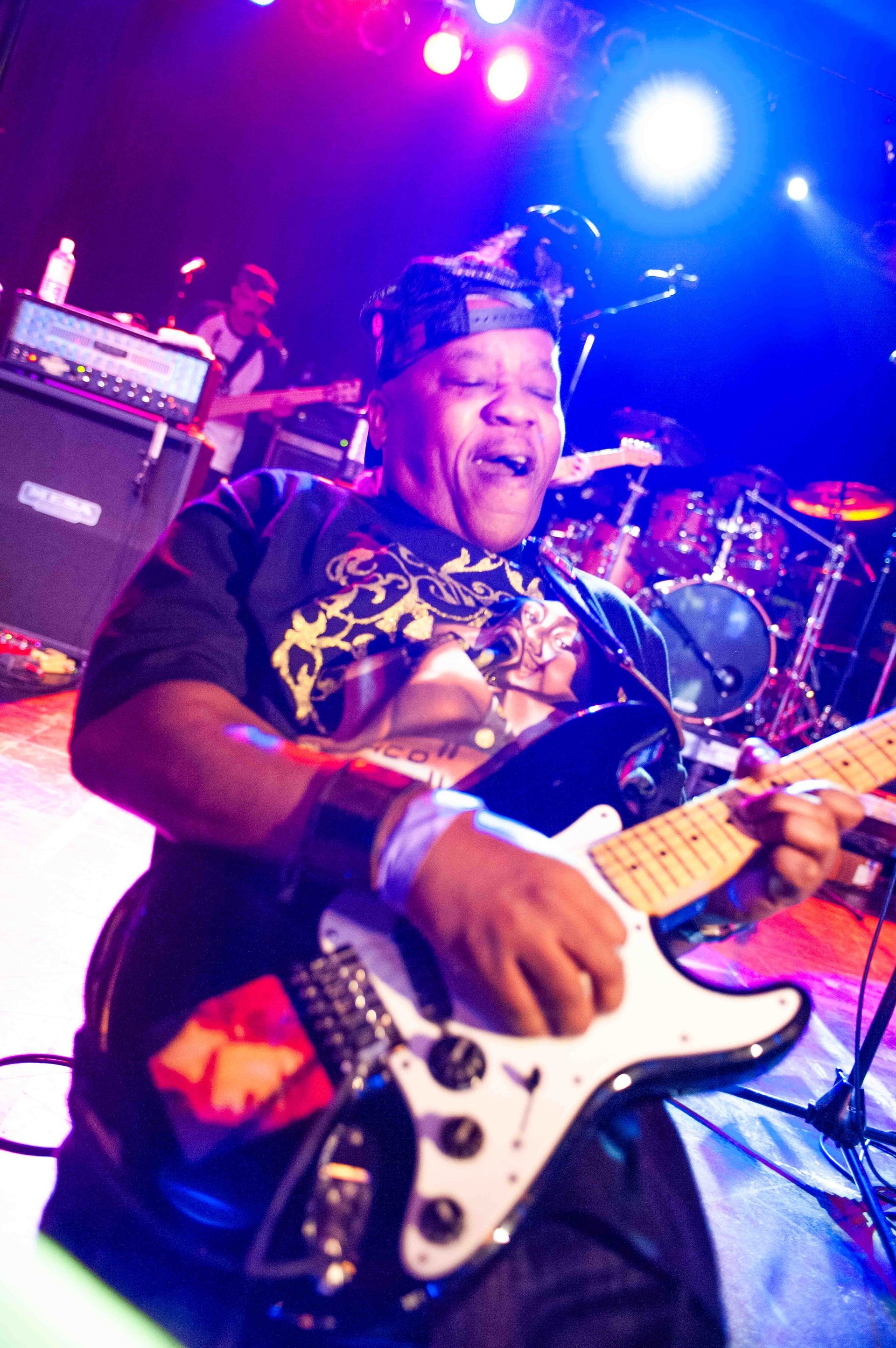 Musician playing electric guitar onstage under purple and blue concert lights