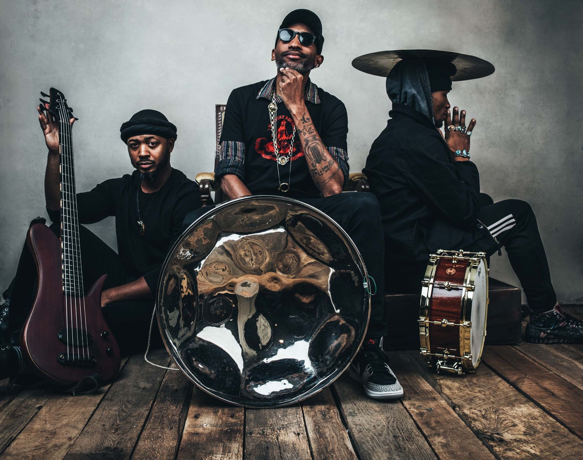 Three musicians posing with guitars, drum, and a brass horn in a moody studio setting