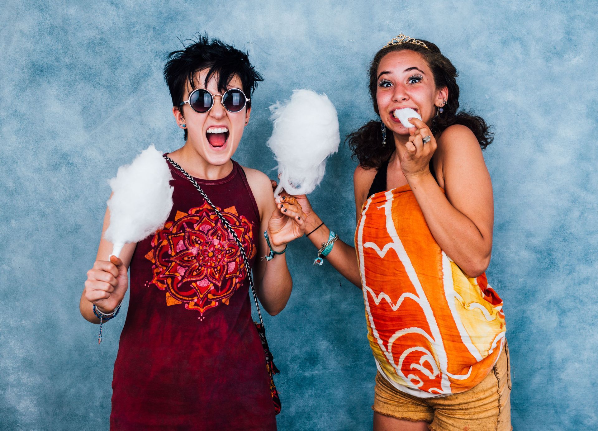 Two people laughing and holding cotton candy against a blue backdrop