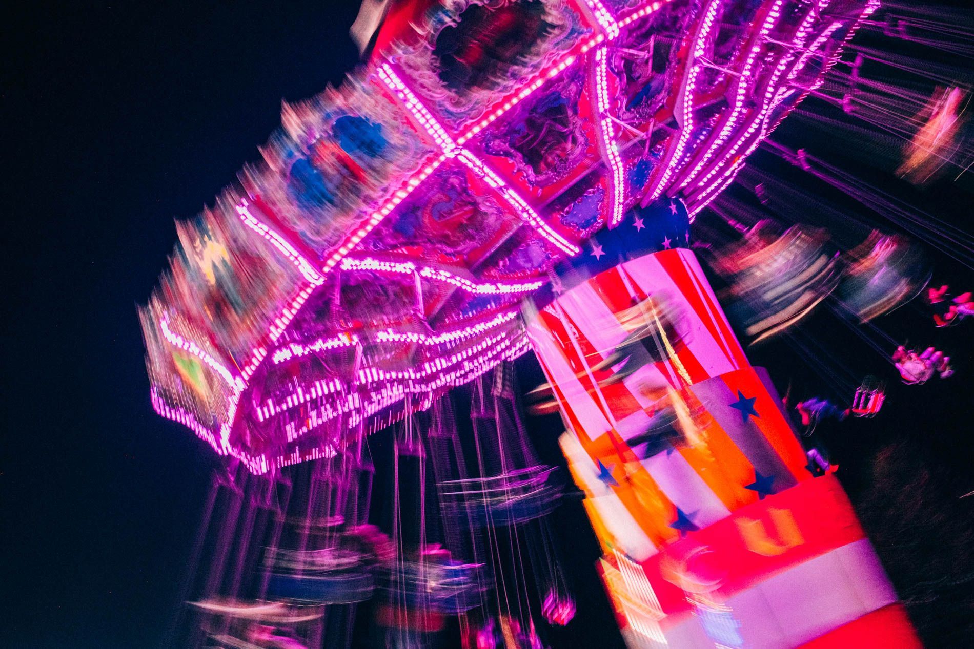 Blurred neon Ferris wheel at night with pink lights and a colorful ride, fine art print from Asheville photographer Sandlin Gaither 