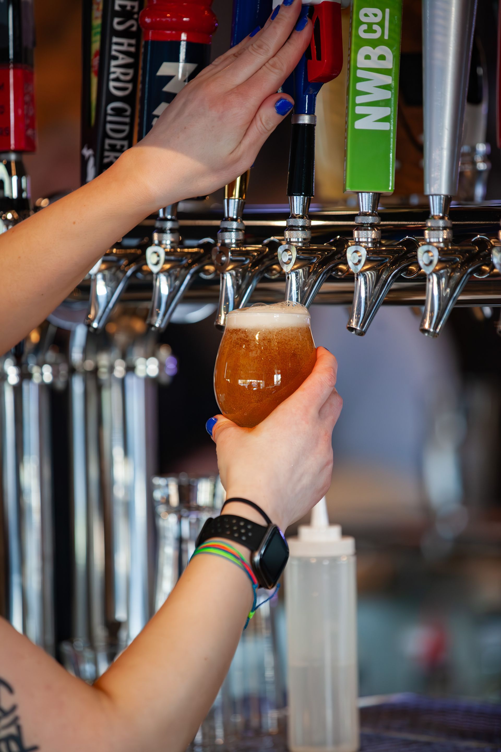A row of glasses filled with beer being poured from a tap.
