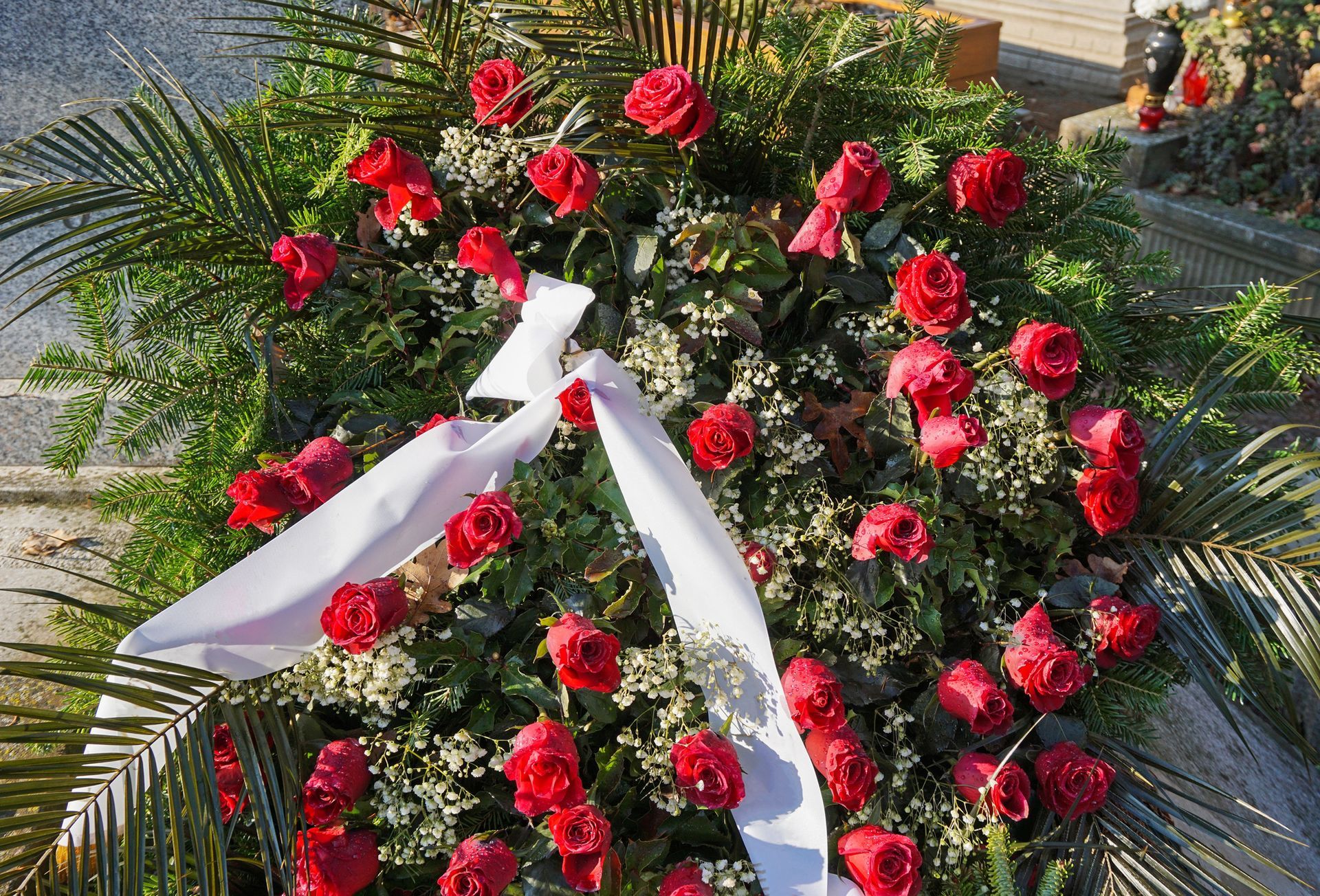 Red floral wreath with white ribbon laid on palm fronds outdoors