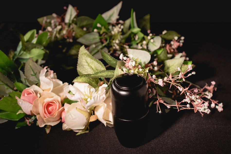 Black perfume bottle surrounded by pink and white roses and green leaves on a dark surface