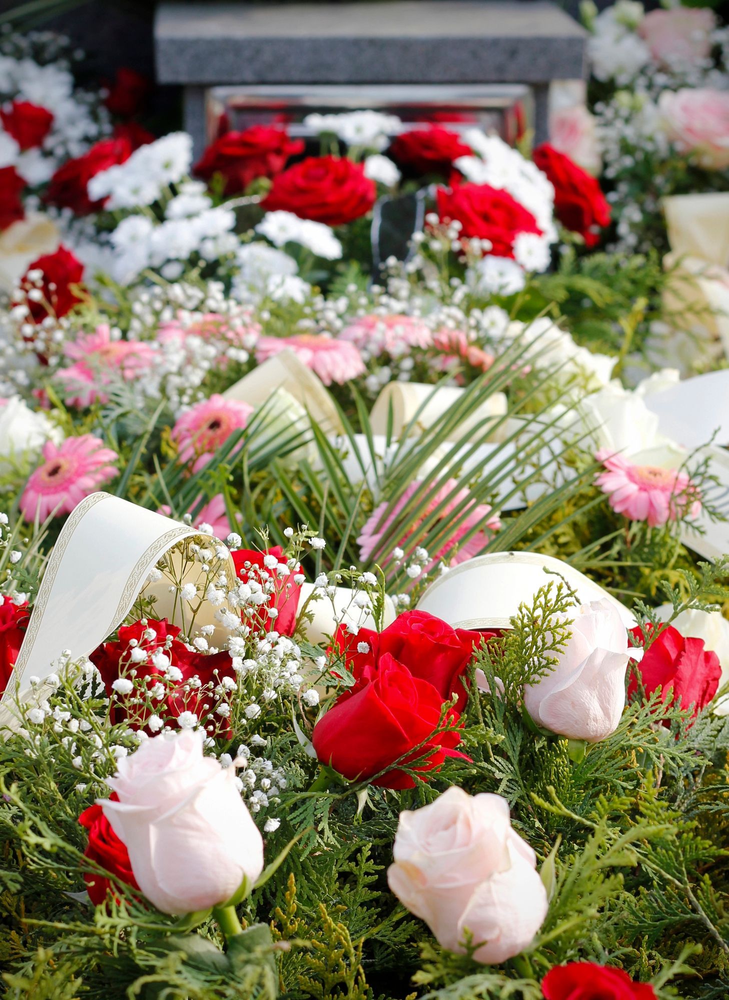 Floral funeral wreaths with red and white roses arranged around a gravestone