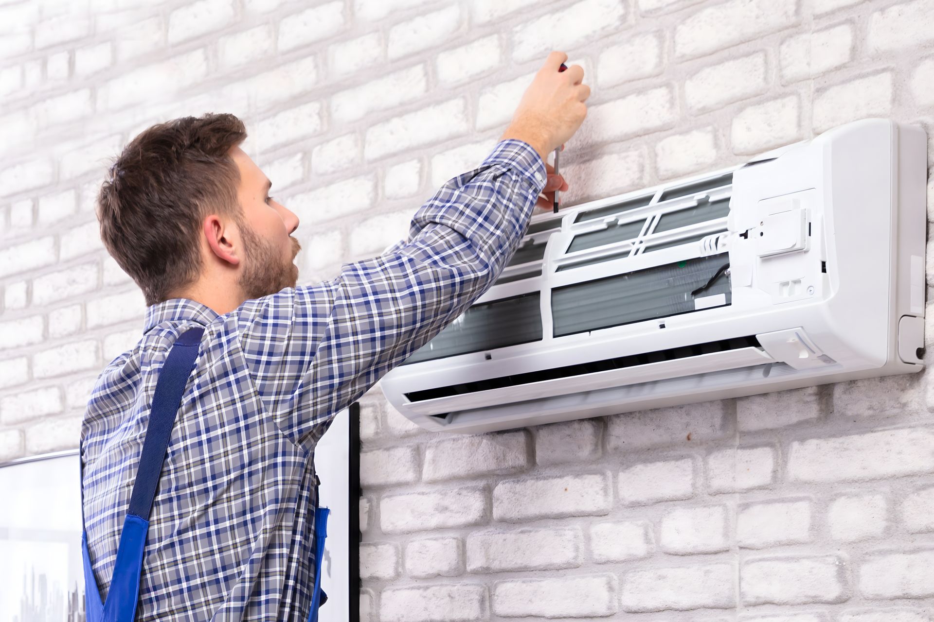 A technician wearing blue overalls is conducting AC repairs on an air conditioner with expert care. A technician wearing blue overalls is conducting AC repairs on an air conditioner with expert care.