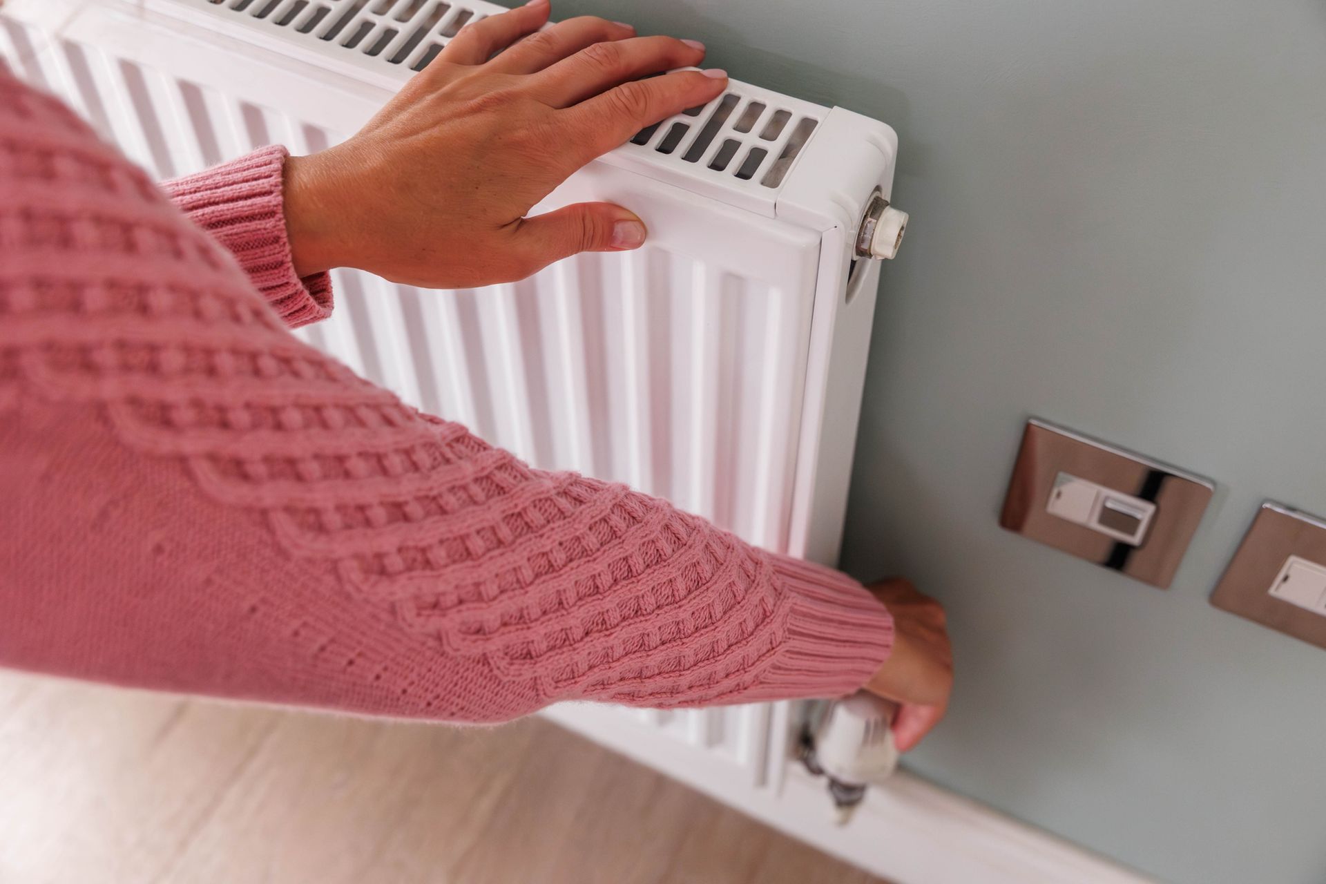 Person adjusting radiator valve during heating system installation in a home.