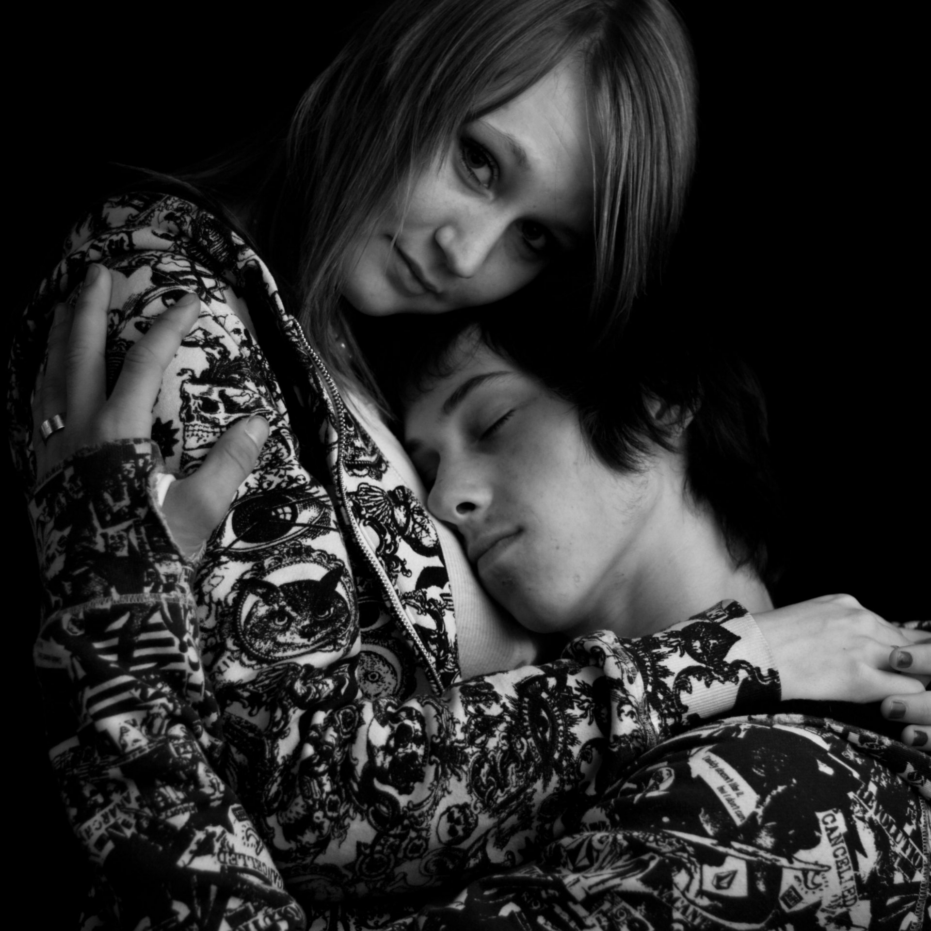 Woman embracing person, face resting on chest. Both wear patterned clothing. Black and white.