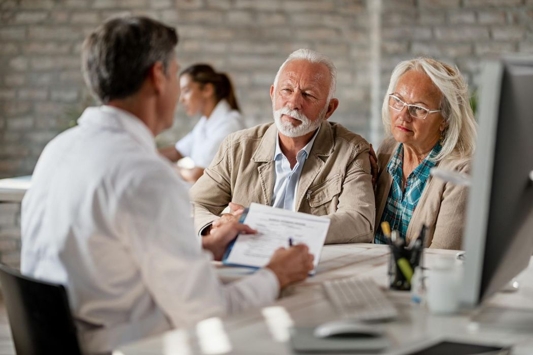 Three people in a meeting reviewing documents at a table in a brick-walled office