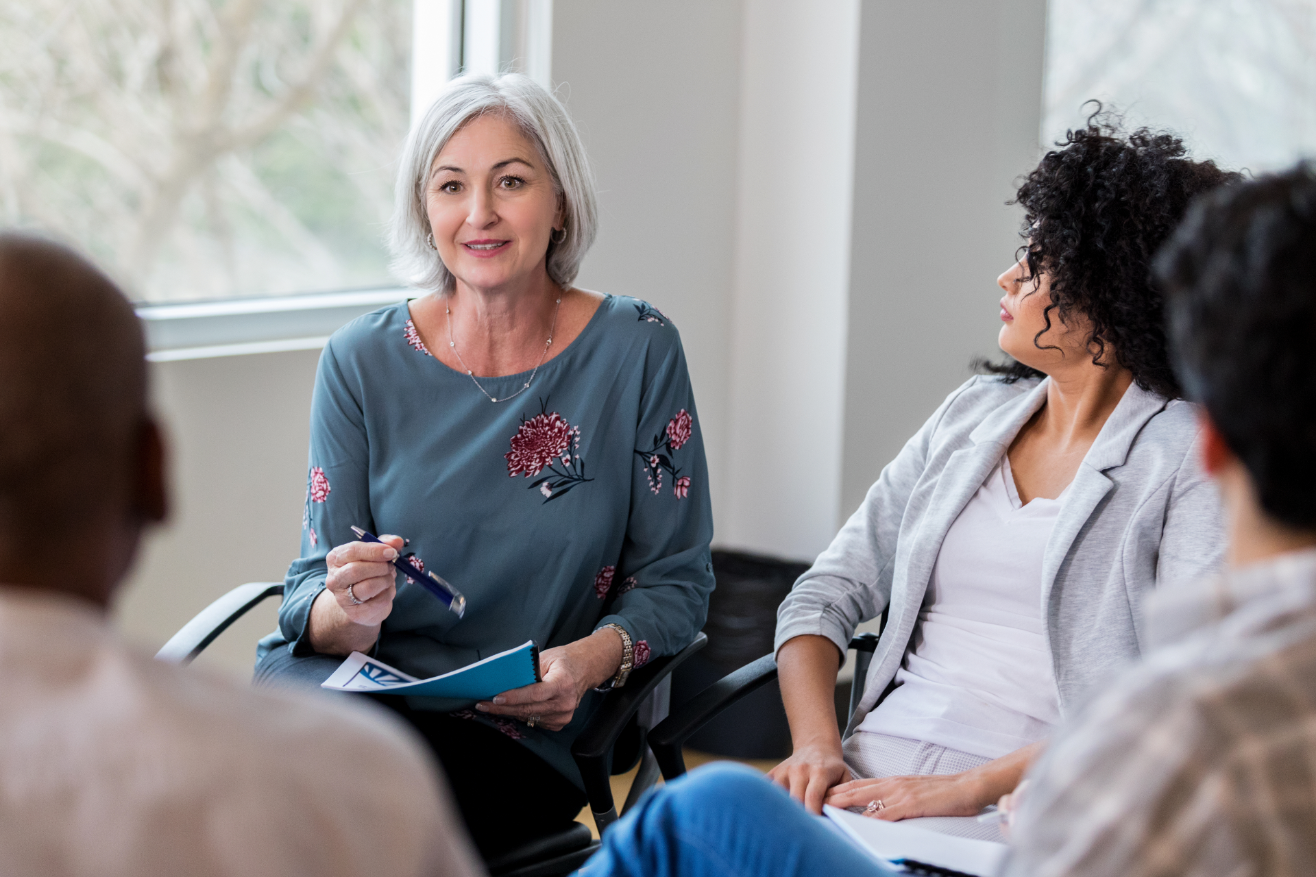 Small group meeting with a woman taking notes and speaking in a bright room