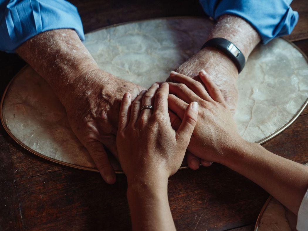 Three hands clasped together over a round table in a close-up view