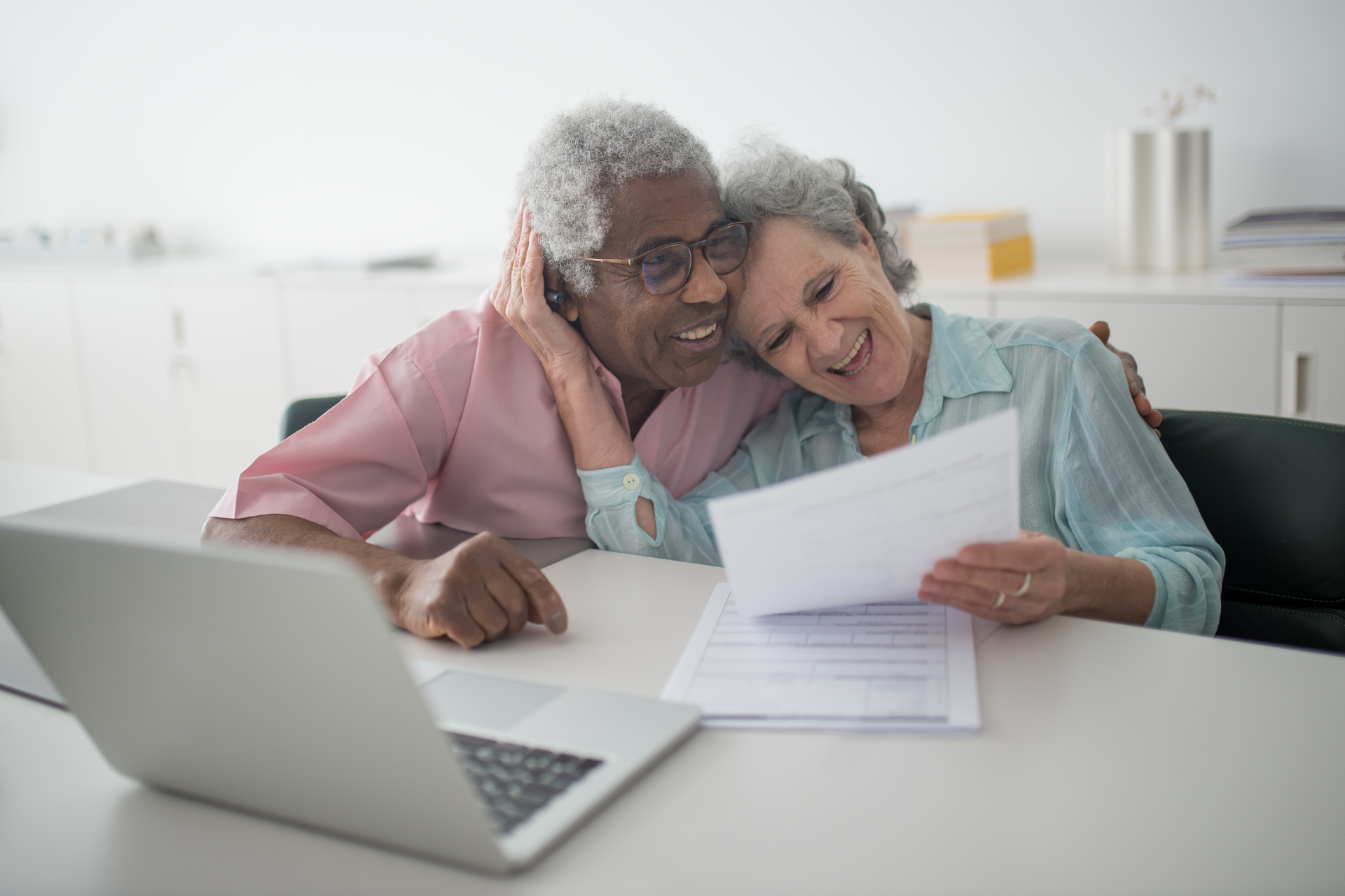 Two people smiling at papers beside a laptop in a bright office