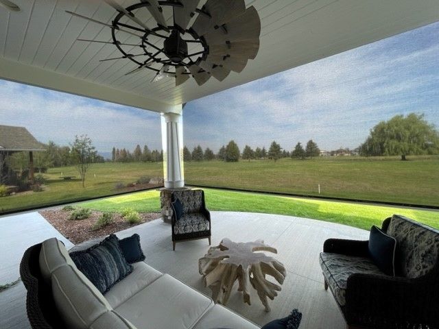 Covered outdoor patio with screen walls and views of a green lawn and blue sky. Furnished with seating and a unique coffee table.
