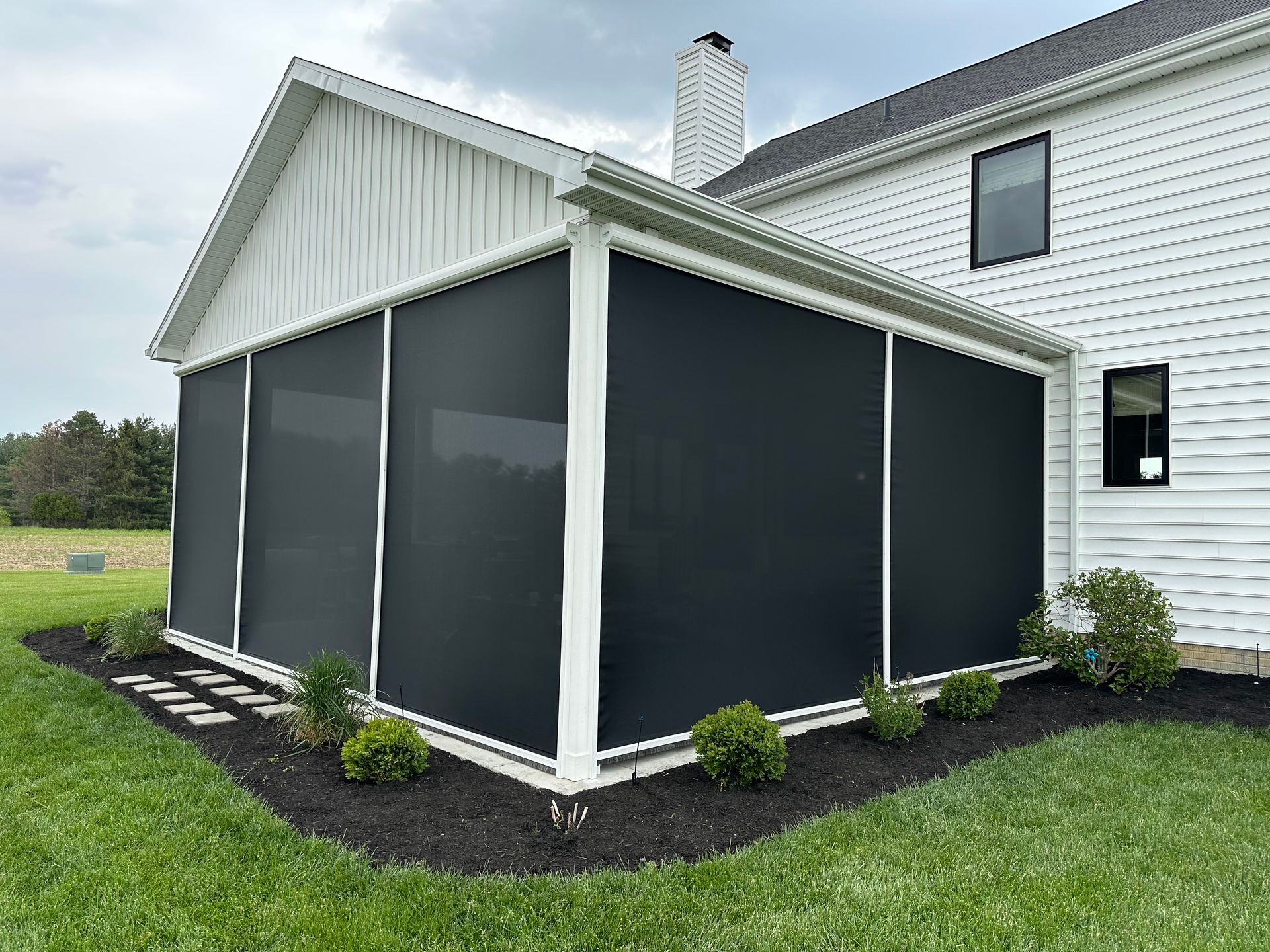Black screened-in porch on a white house. Black screens surround the porch, green grass and bushes in the yard.