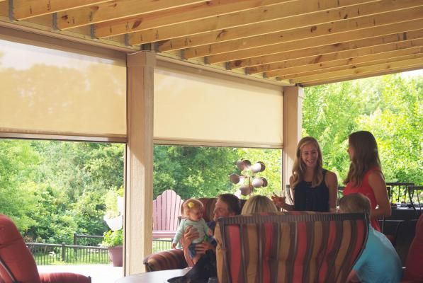 People gathered on a covered patio with shades, enjoying a view of trees.