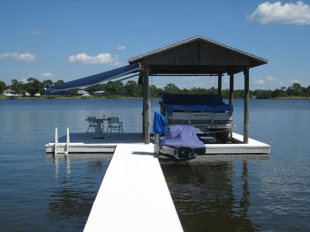 Dock with boat lift, covered boat, and seating area on a lake under a blue sky.