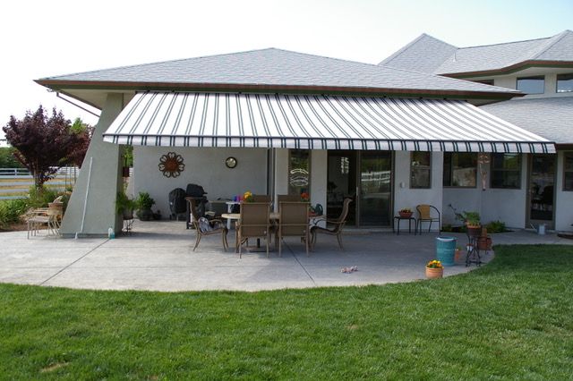 Patio with retractable striped awning over a table and chairs, near a house with grass.