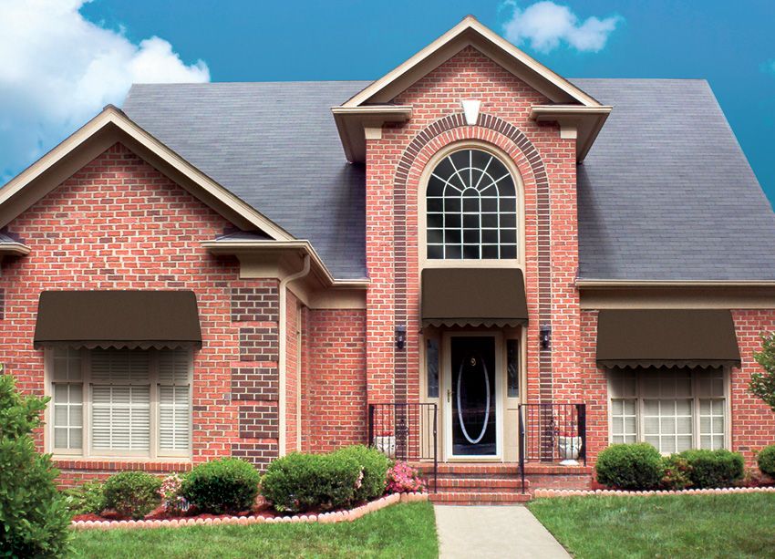 Brick house with brown awnings over windows, a dark roof, and blue sky.