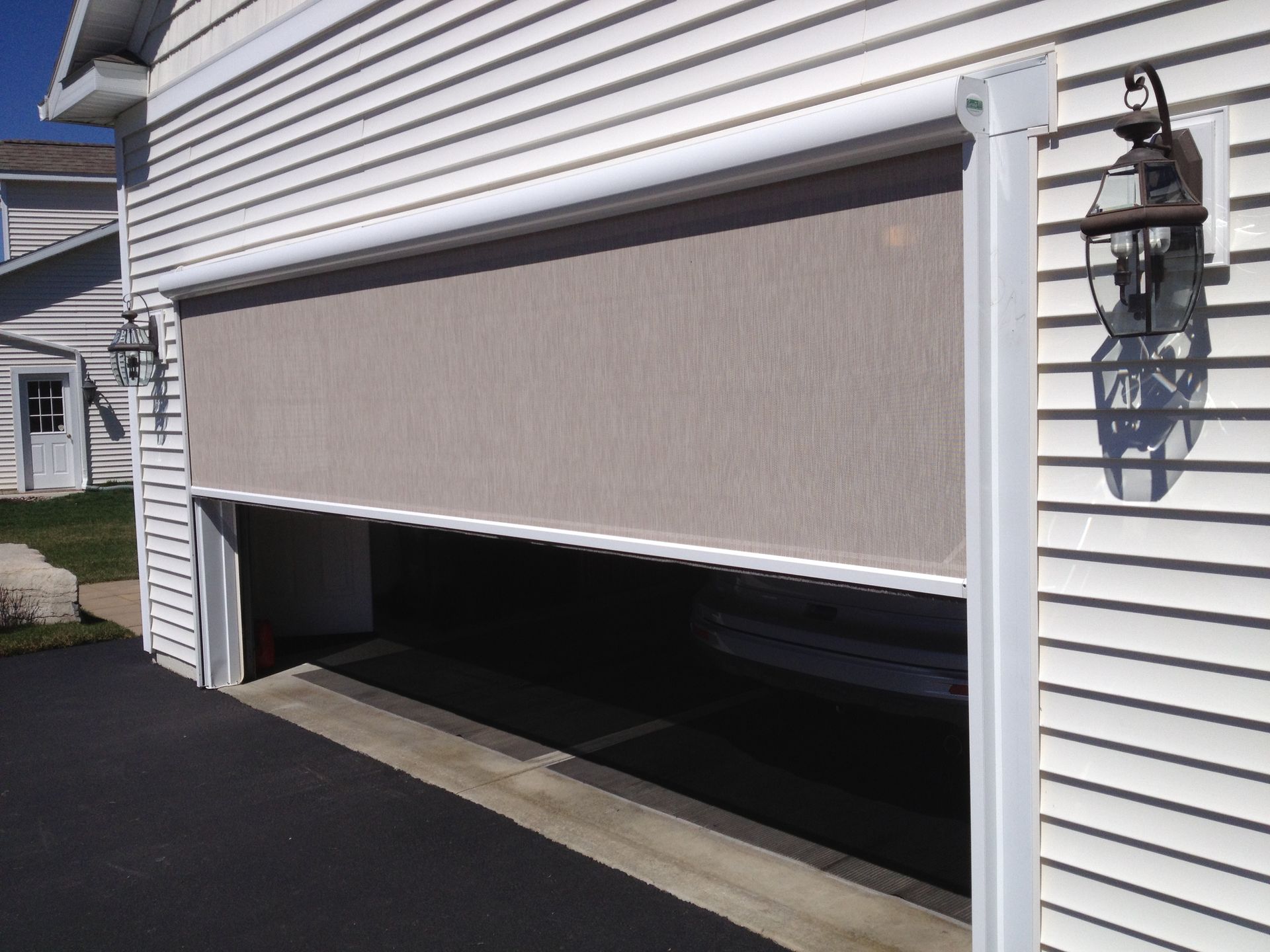Beige screen partially covering an open garage door on a white-sided house.