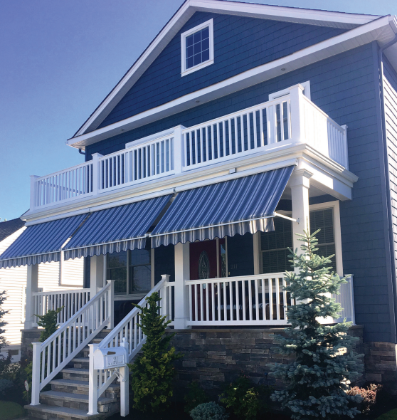 Two-story blue house with white railing, striped awnings over the porch, steps leading up.