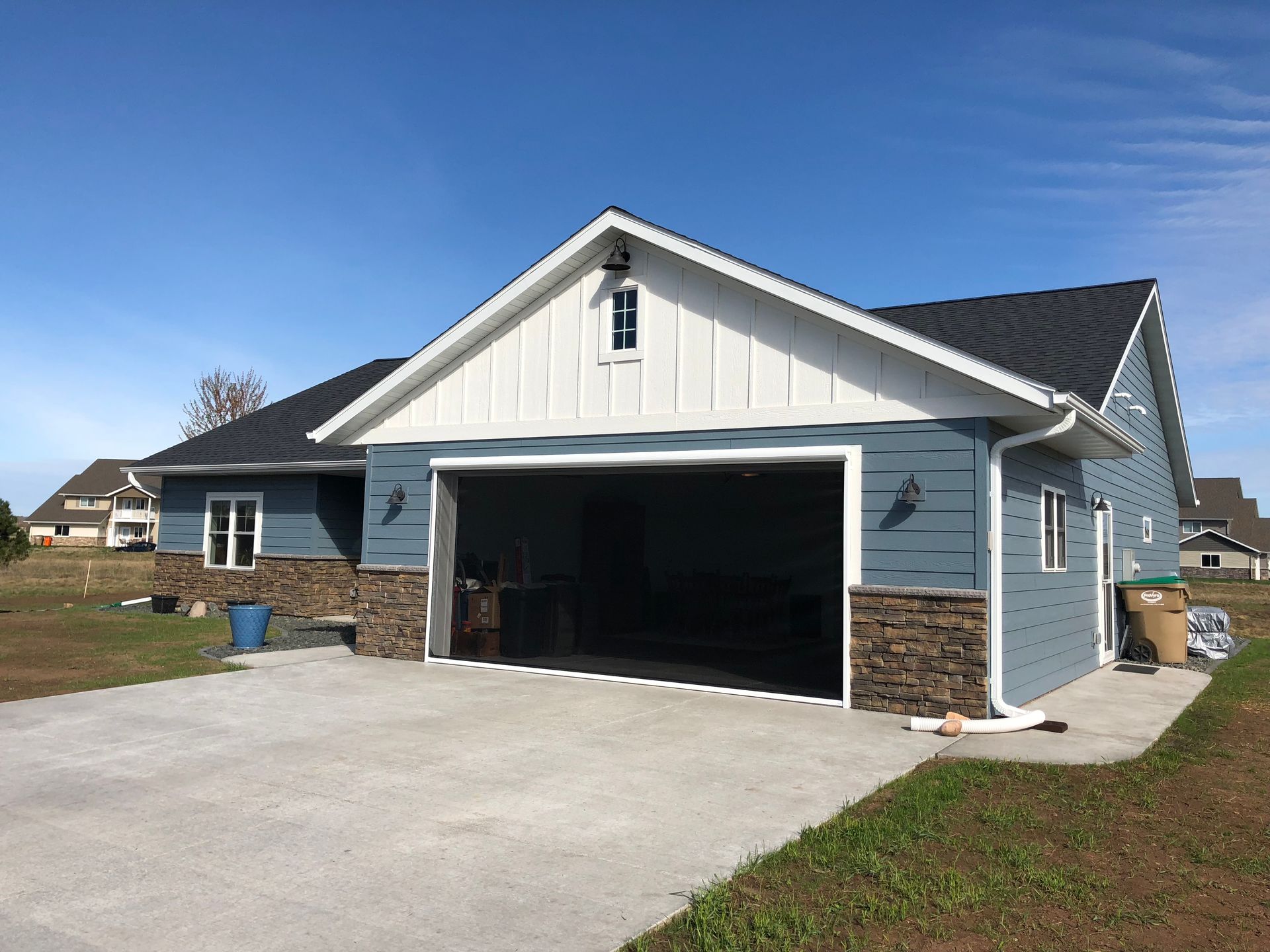 Blue house with open garage and stone veneer base on a concrete driveway, sunny day.