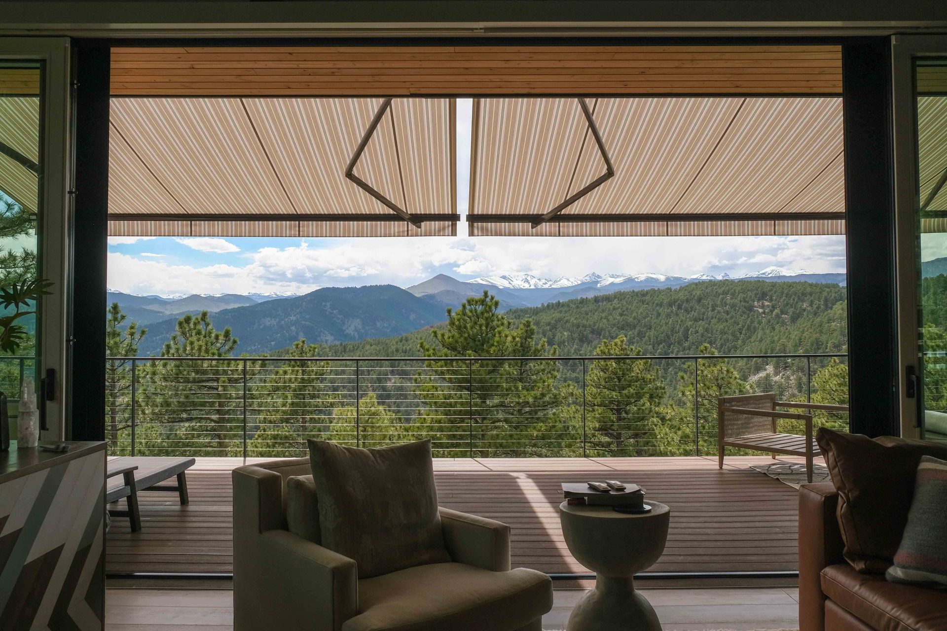 Interior view of a modern home with open sliding doors revealing a mountain view, with beige shades partially drawn.