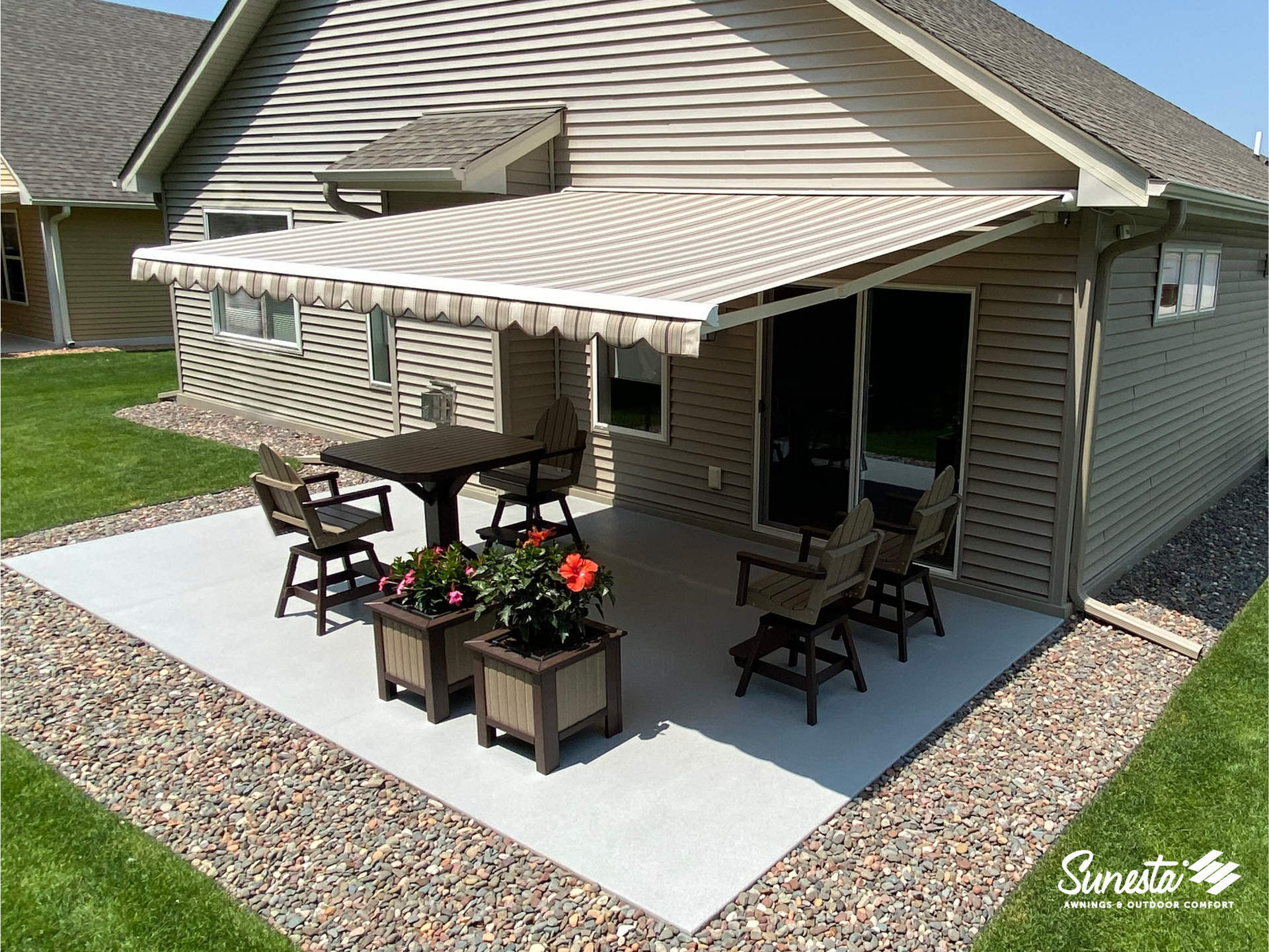 Beige awning over a patio with furniture, flower boxes, and a house.