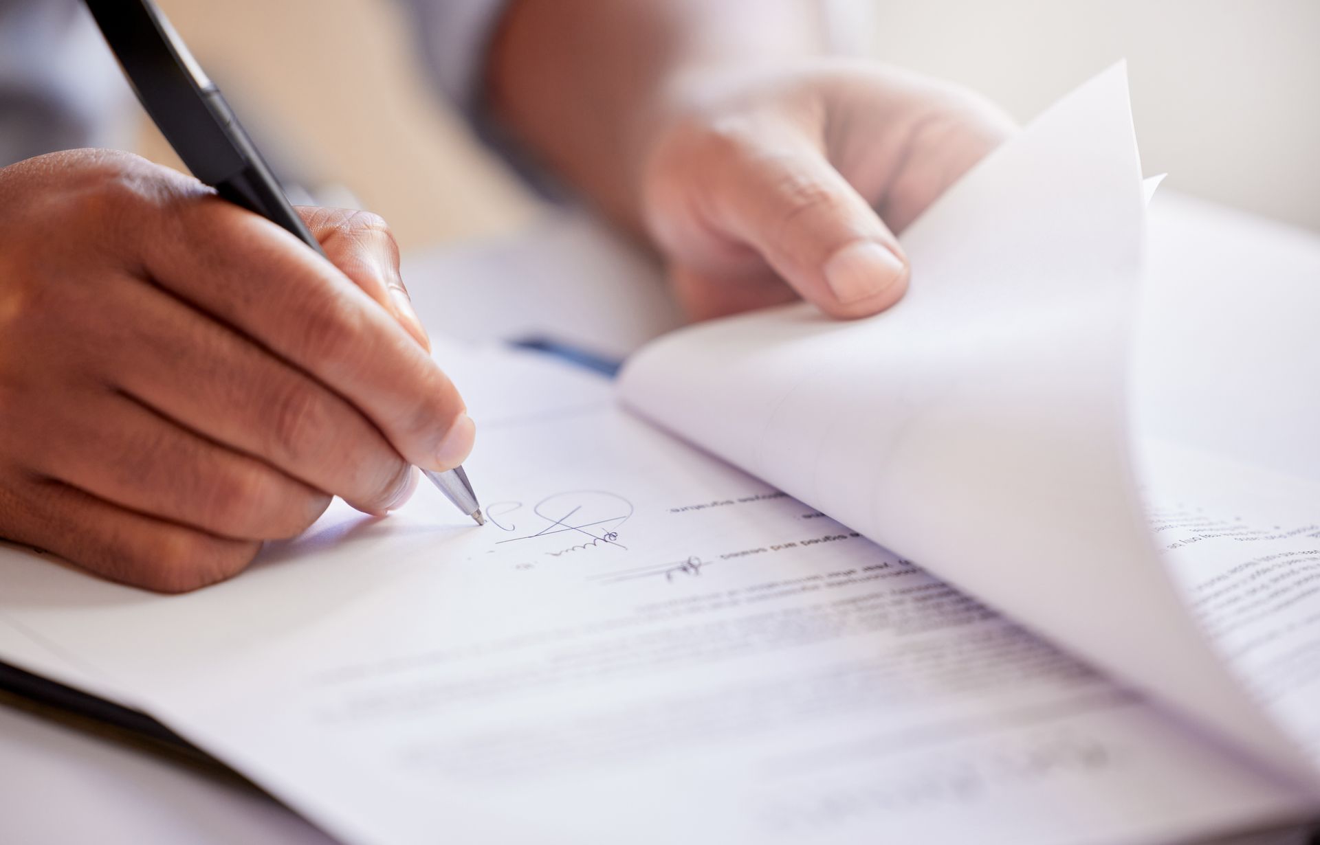 Person's hands signing a document with a pen, holding a stack of papers, close up.