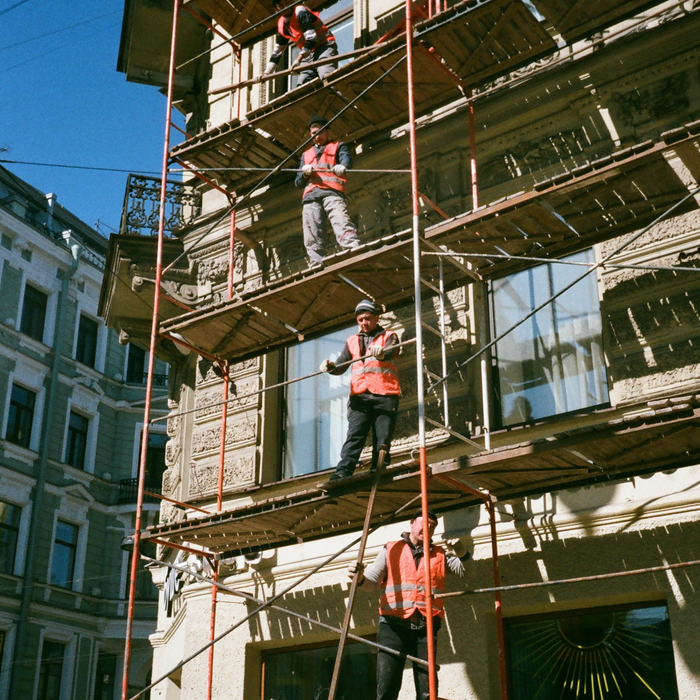 Workers in orange vests on scaffolding, renovating a building with ornate facade.