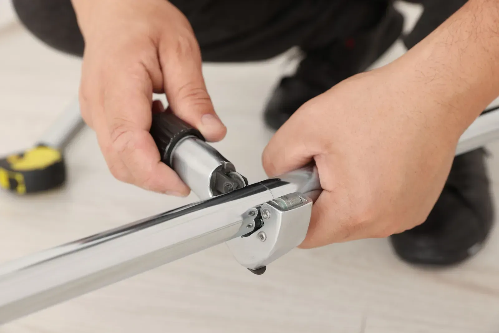 Hands tightening a metal clamp on a silver frame with a black tool