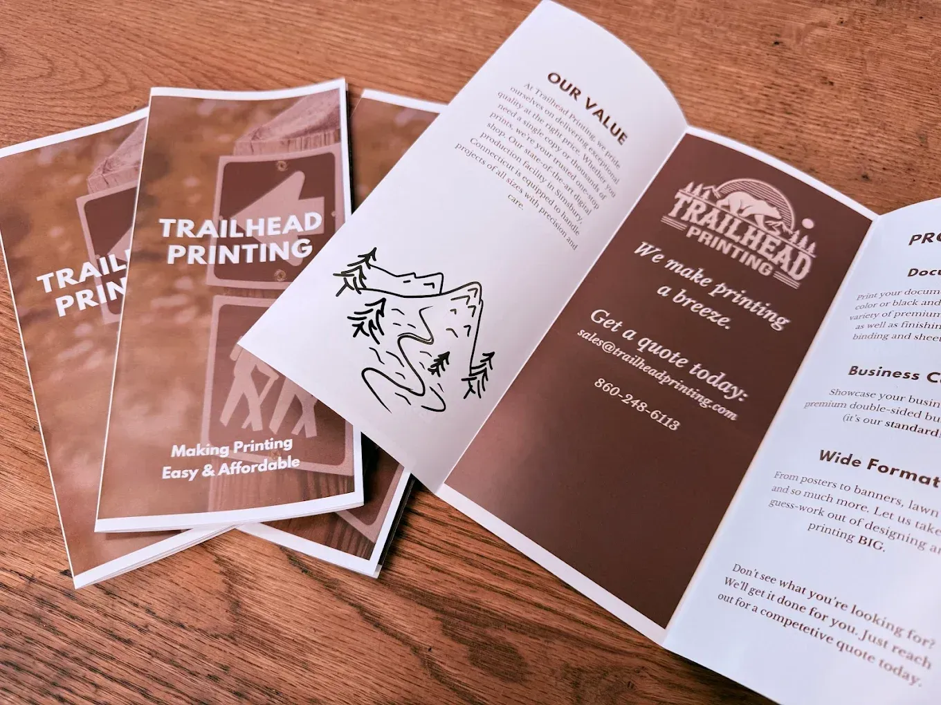 Brochure spread on wooden table showing Trailhead Printing marketing materials in brown and white.