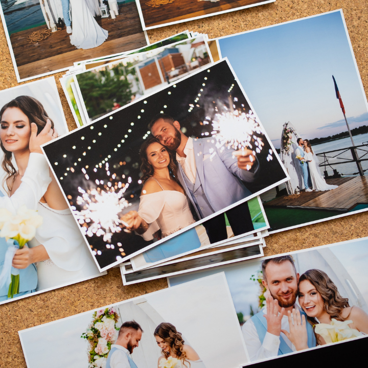 Wedding photos on a corkboard. Couple with sparklers, bride smiling, groom holding hands, waterfront location.