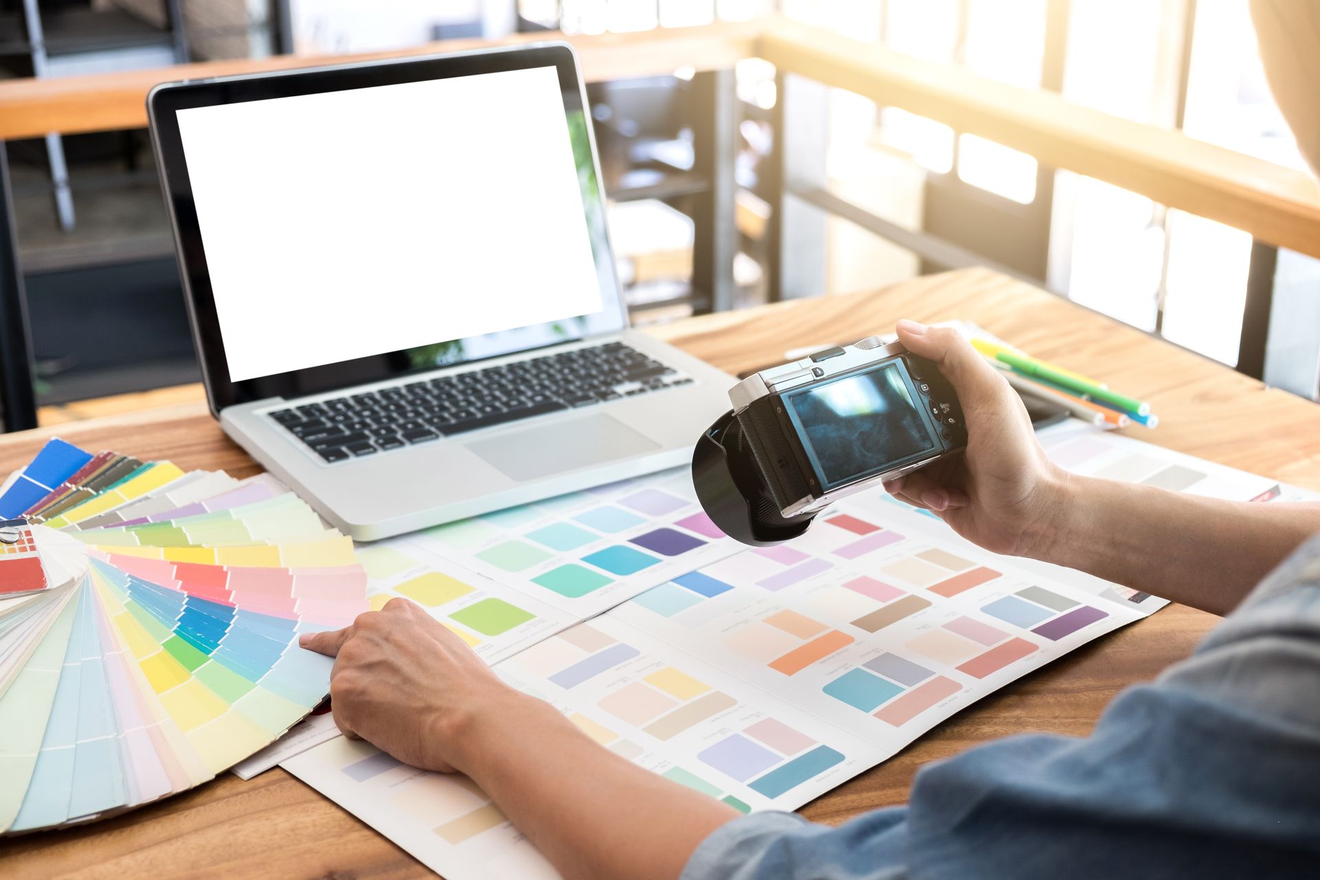 Designer reviewing color swatches and samples beside a laptop, with a handheld scanner on a desk