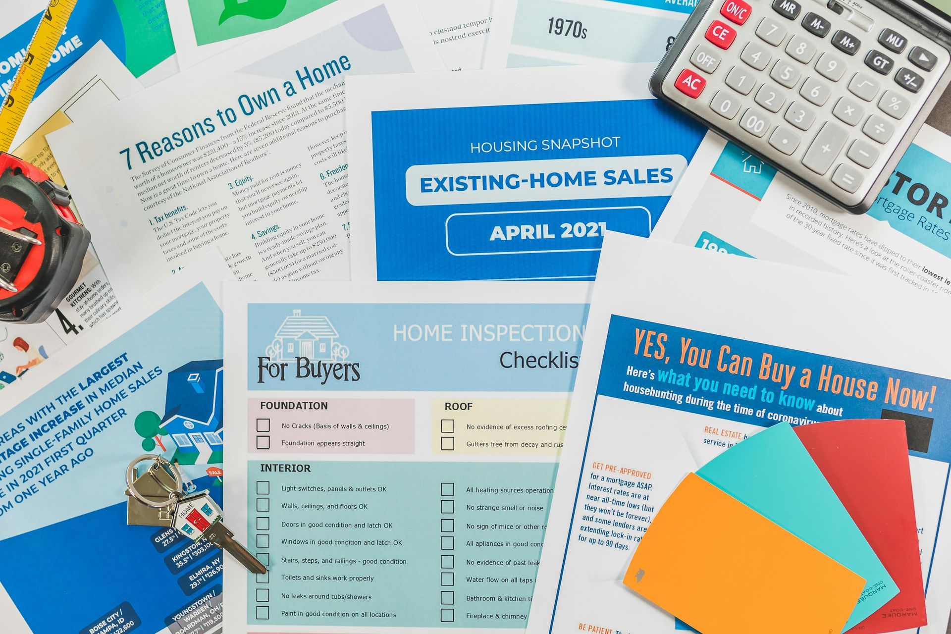 Papers, calculator, keys, and color swatches on a desk, related to home buying and inspection.
