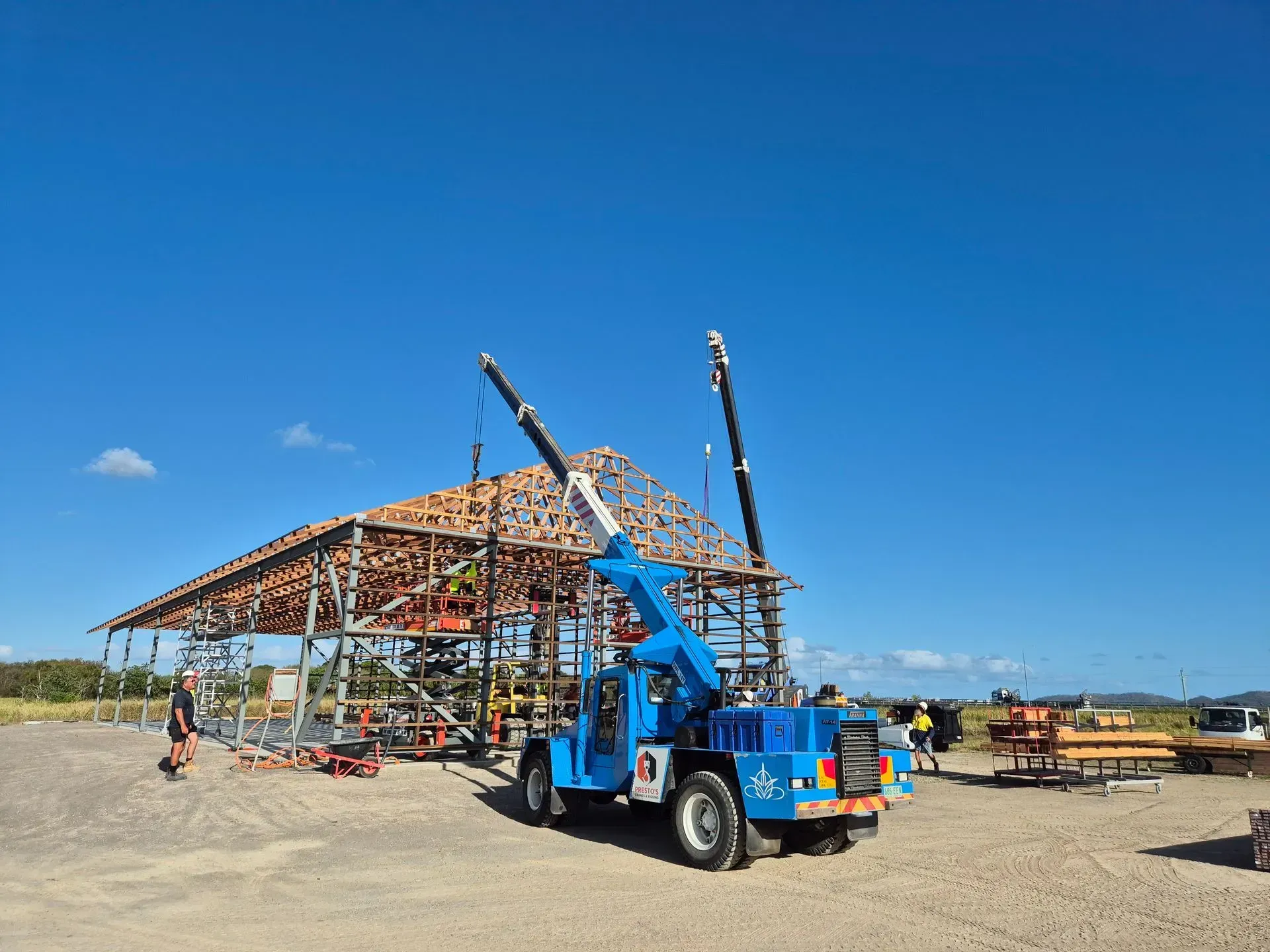 Blue Crane Lifting Roof Trusses on a Building Frame — Presto's Cranes & Rigging NQ in Garbutt, QLD