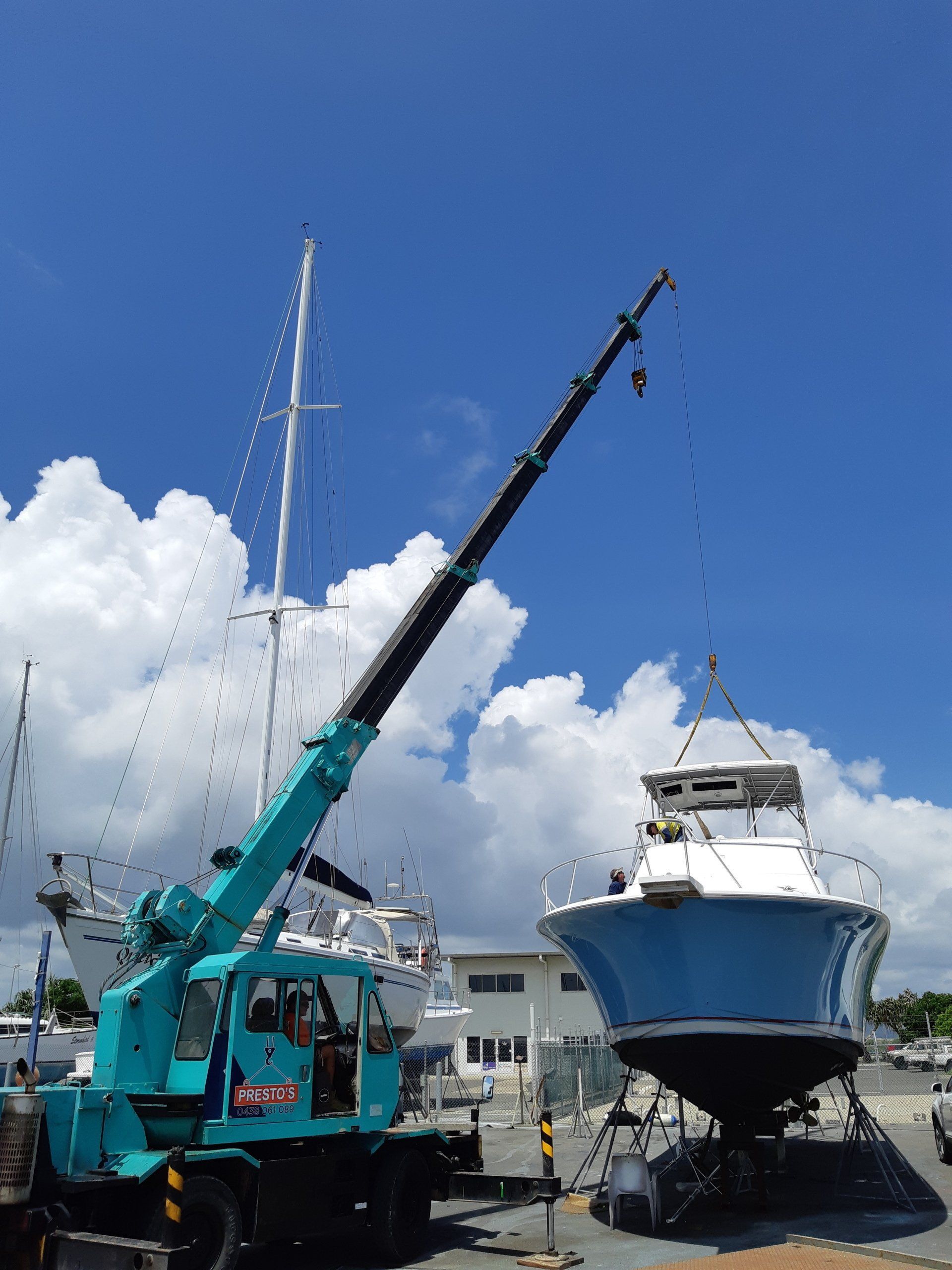 A Crane Lifting a Blue and White Boat at a Marina — Presto's Cranes & Rigging NQ in Garbutt, QLD