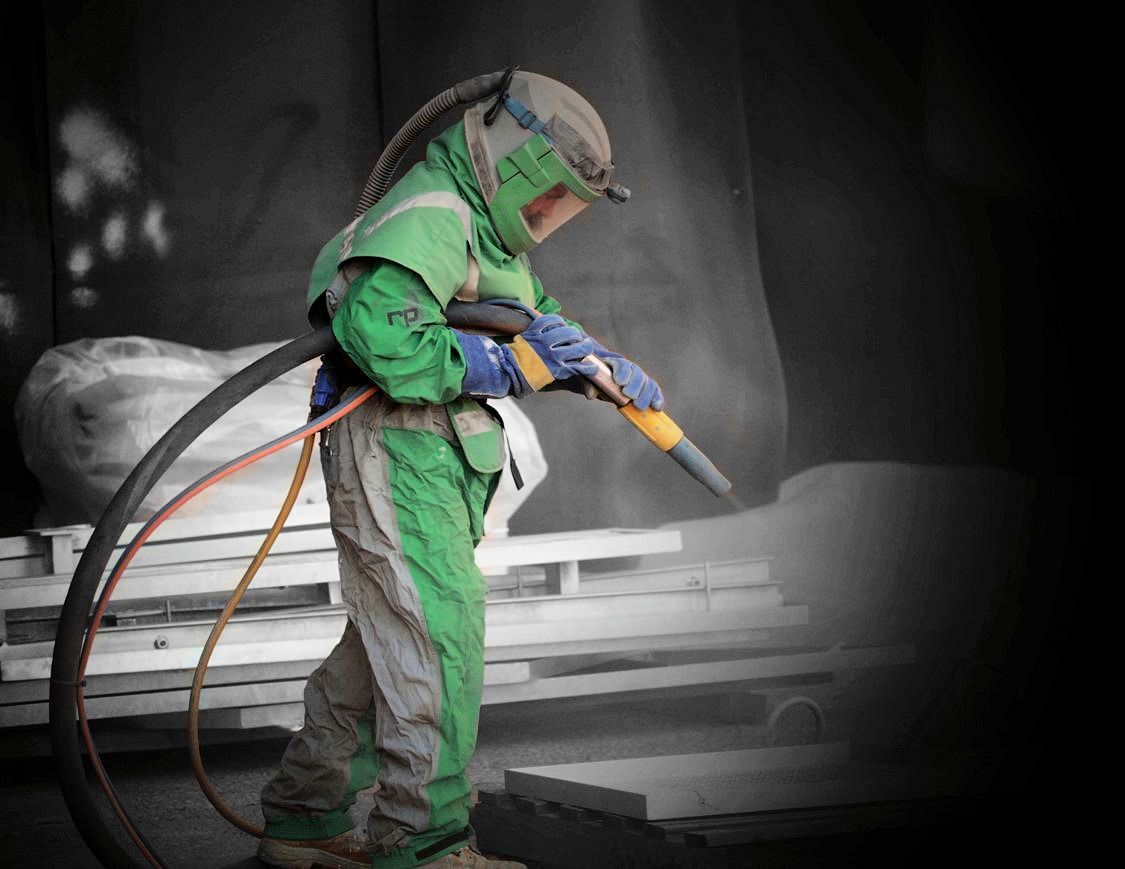A Man In A Green Suit Is Sandblasting A Piece Of Metal — JMG Maintenance & Fabrication In Muswellbrook NSW