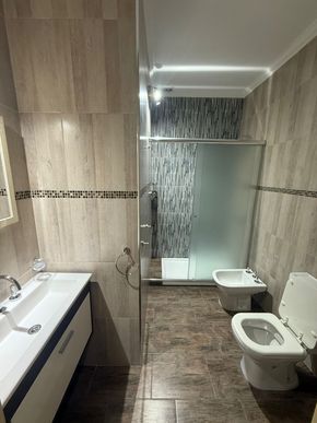 Baño con ducha, inodoro y bidé. Azulejos beige y marrón, lavabo y grifería blancos.