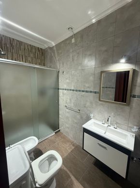 Baño con paredes de azulejos grises, ducha de vidrio esmerilado, inodoro blanco y lavabo flotante.
