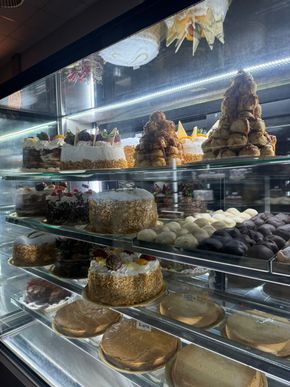 Vitrina de pastelería llena de diversos pasteles, tartas y delicias, iluminada por luz cenital.
