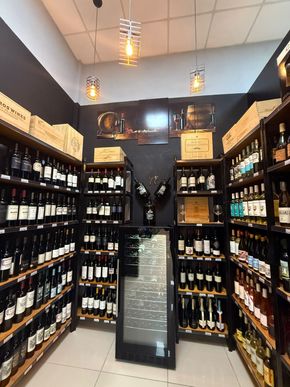 Interior de tienda de vinos con filas de botellas de vino en estantes de madera, paredes negras e iluminación decorativa.